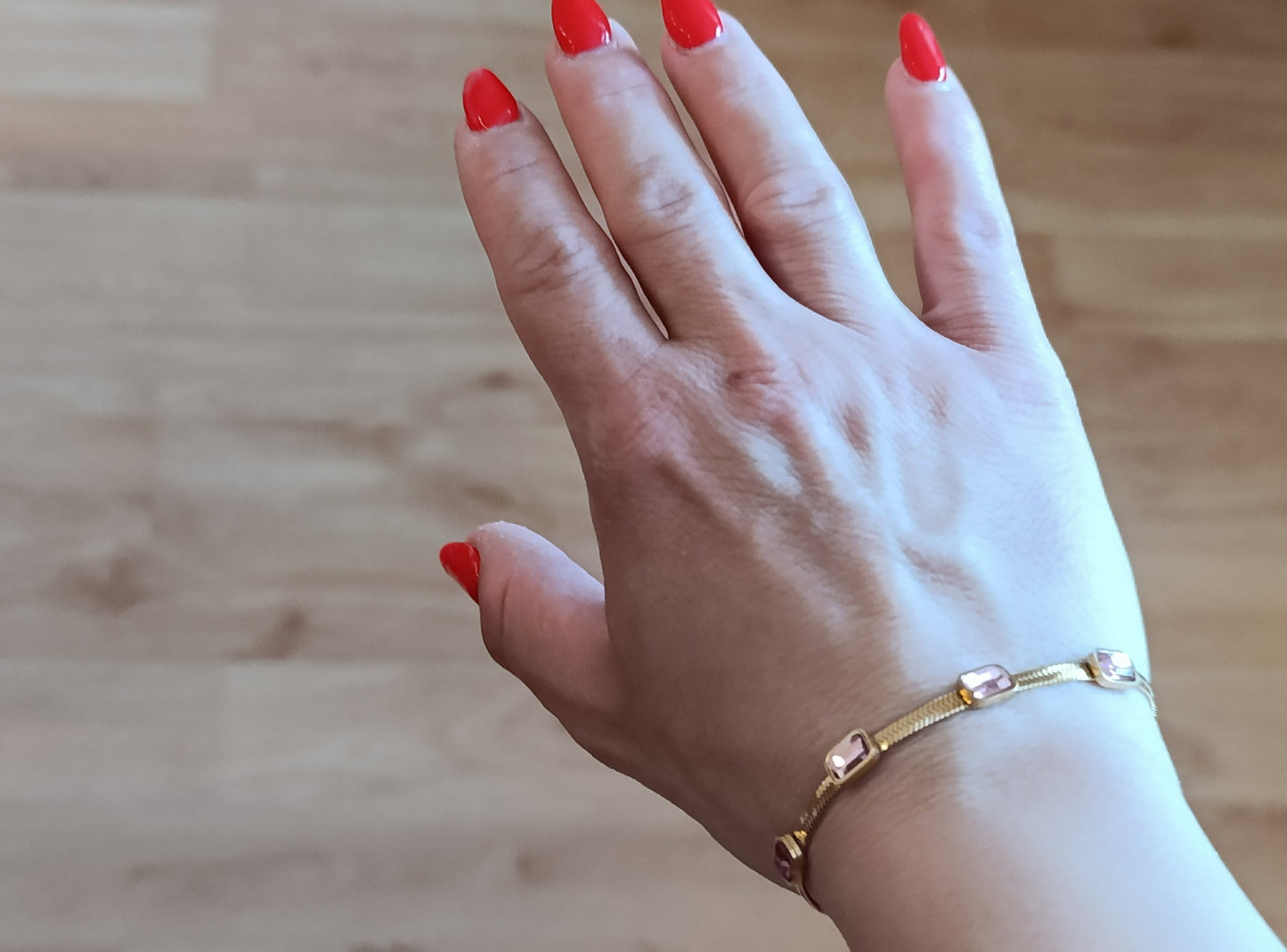 Χρυσό stainless steel βραχιόλι φορεμένο στον καρπό με ροζ ορθογώνια κρύσταλλα και λεπτή επίπεδη αλυσίδα.